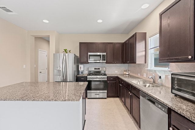 212 Timber Brook Dr, Hutto, TX 78634 - kitchen with decorative backsplash, dark brown cabinets, light stone counters, a sink, and appliances with stainless steel finishes