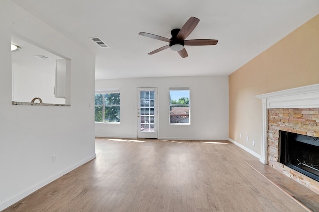 unfurnished living room featuring light hardwood / wood-style flooring, a stone fireplace, and ceiling fan