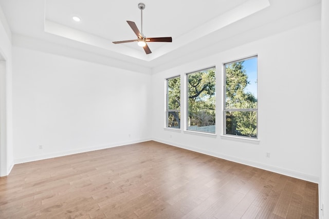 spare room featuring a raised ceiling, ceiling fan, and light hardwood / wood-style floors