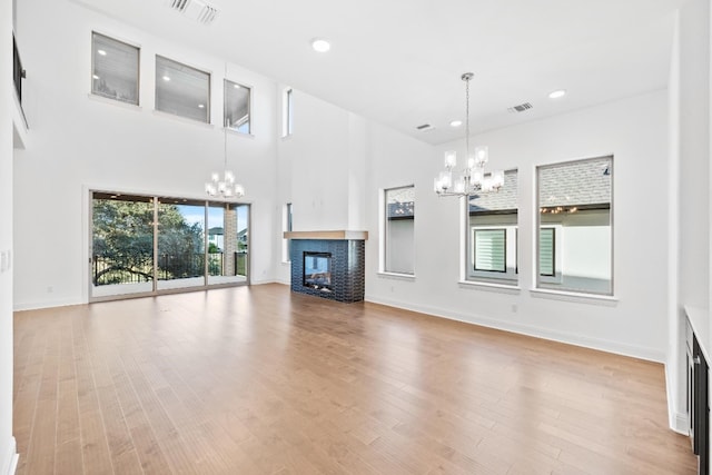 unfurnished living room featuring a multi sided fireplace, light hardwood / wood-style flooring, a high ceiling, and an inviting chandelier