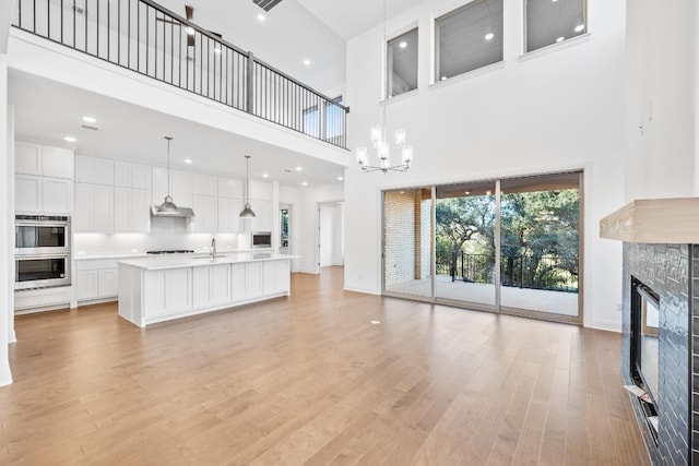 living room featuring a stone fireplace, sink, a high ceiling, and light hardwood / wood-style flooring