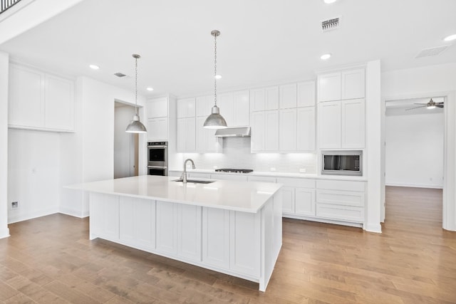 kitchen featuring a center island with sink, white cabinets, exhaust hood, and sink