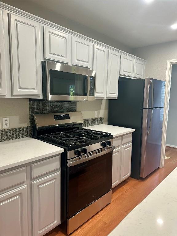 kitchen featuring tasteful backsplash, white cabinets, stainless steel appliances, and light hardwood / wood-style floors