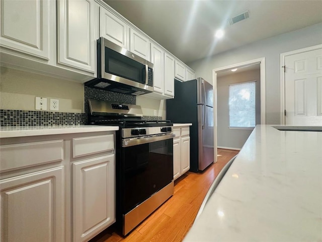 kitchen with decorative backsplash, light stone countertops, light wood-type flooring, stainless steel appliances, and white cabinets