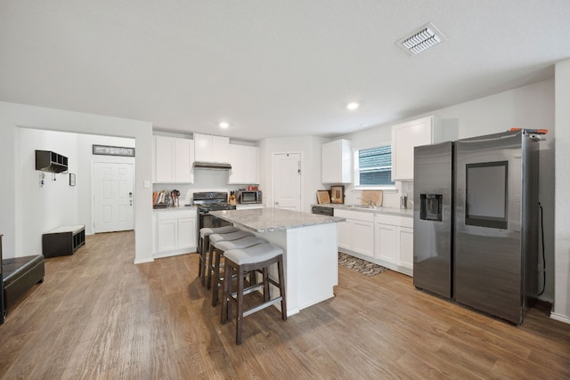 kitchen featuring hardwood / wood-style flooring, a kitchen island, white cabinetry, and stainless steel appliances