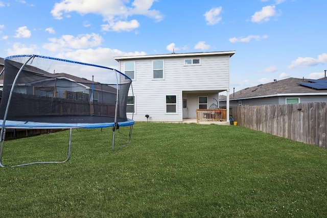 back of property with a trampoline and a yard