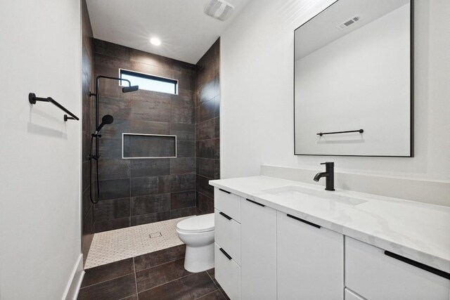 bathroom with tiled shower, tile patterned floors, vanity, and toilet