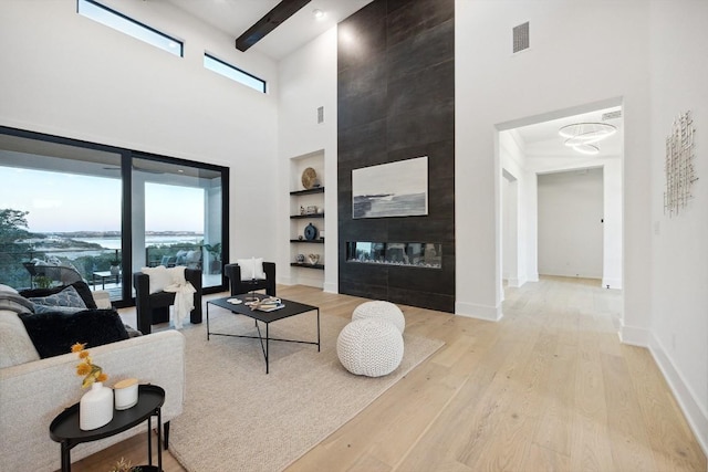 living room featuring light wood-type flooring, built in shelves, a towering ceiling, and a fireplace