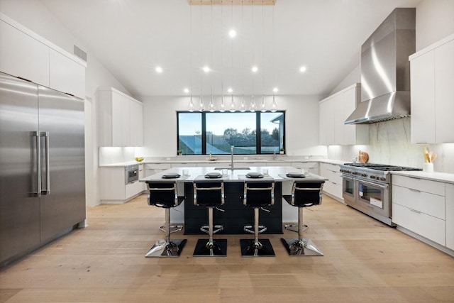 kitchen with a kitchen bar, wall chimney exhaust hood, high end appliances, and white cabinetry