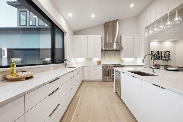 kitchen featuring appliances with stainless steel finishes, wall chimney exhaust hood, pendant lighting, white cabinets, and lofted ceiling