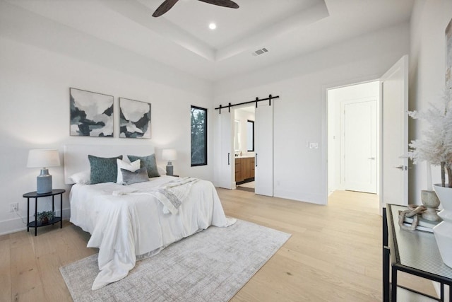 18116 Cedar Sage Ct, Lago Vista, TX 78645 - bedroom featuring light wood finished floors, a barn door, a raised ceiling, baseboards, and recessed lighting
