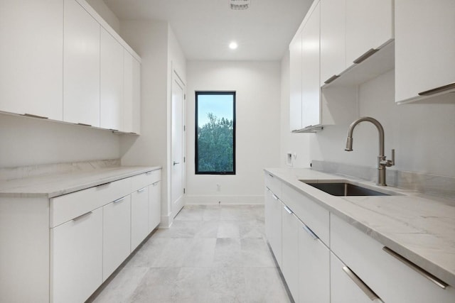 kitchen with light stone counters, white cabinetry, and sink