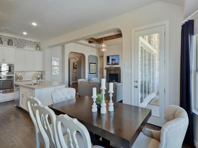 20517 Martin Ln, Pflugerville, TX 78660 - dining room featuring arched walkways, dark wood-style flooring, recessed lighting, a stone fireplace, and beamed ceiling