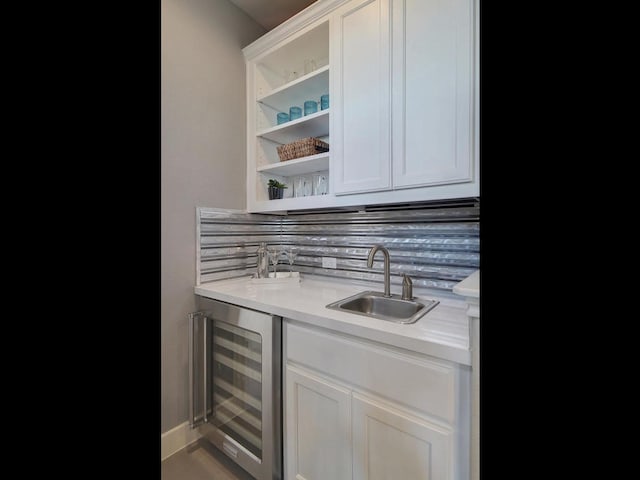 bar with beverage cooler, white cabinets, sink, and tasteful backsplash