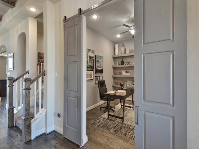 home office with a barn door, ceiling fan, and dark hardwood / wood-style floors