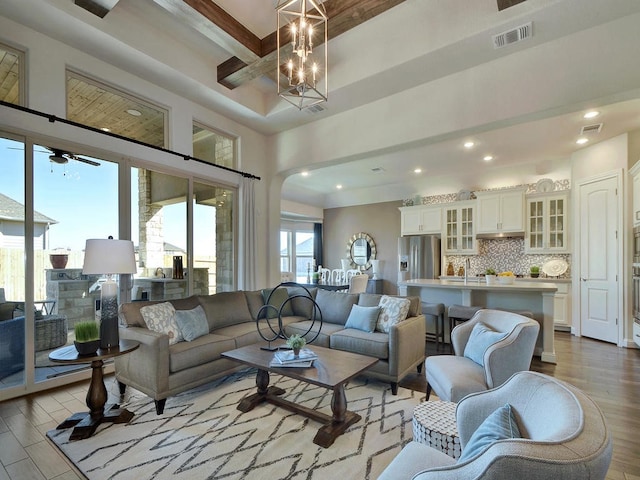 living room with a tray ceiling, light hardwood / wood-style floors, sink, and ceiling fan with notable chandelier