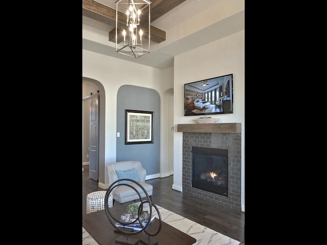 living room featuring beamed ceiling, a notable chandelier, dark wood-type flooring, and a brick fireplace