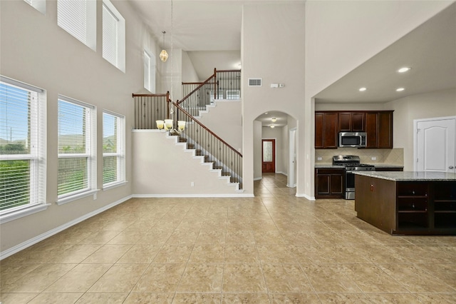 kitchen with dark brown cabinetry, stainless steel appliances, a high ceiling, light stone counters, and backsplash