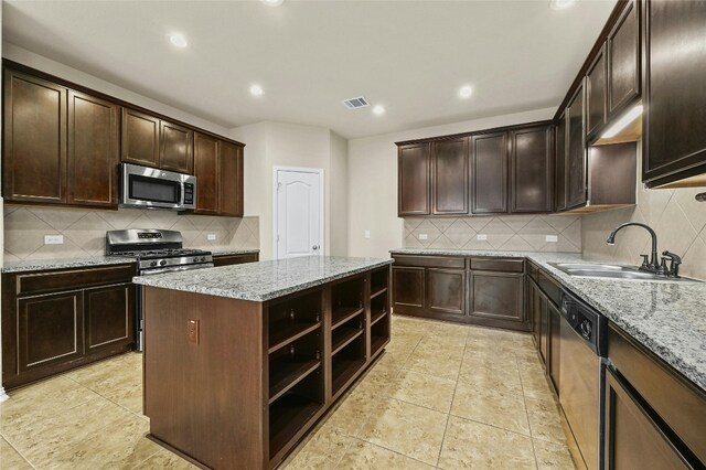 kitchen with light stone counters, sink, a center island, and appliances with stainless steel finishes