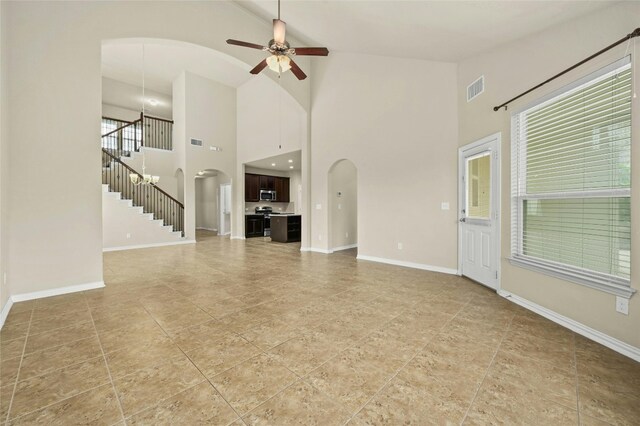 unfurnished living room featuring a wealth of natural light, ceiling fan, and a high ceiling