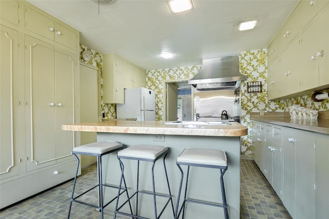 kitchen with a kitchen bar, white refrigerator, a kitchen island, and exhaust hood