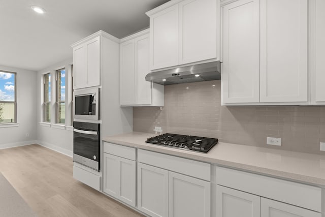 kitchen with light hardwood / wood-style flooring, appliances with stainless steel finishes, white cabinets, exhaust hood, and decorative backsplash