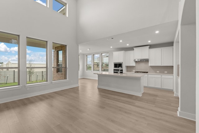 kitchen with white cabinets, tasteful backsplash, black gas stovetop, a center island with sink, and light hardwood / wood-style floors