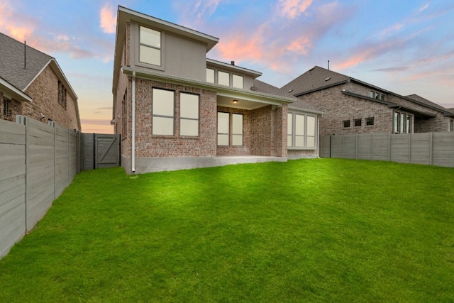 back house at dusk with a patio area and a yard