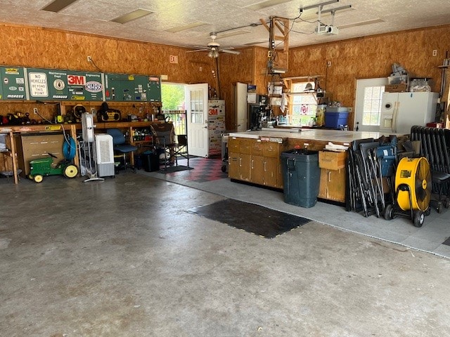 garage featuring a workshop area, ceiling fan, white fridge with ice dispenser, and a garage door opener