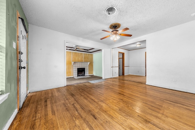 unfurnished living room featuring ceiling fan, a tile fireplace, a textured ceiling, and hardwood / wood-style flooring