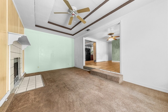 unfurnished living room with a tray ceiling, ceiling fan, carpet floors, and a tiled fireplace