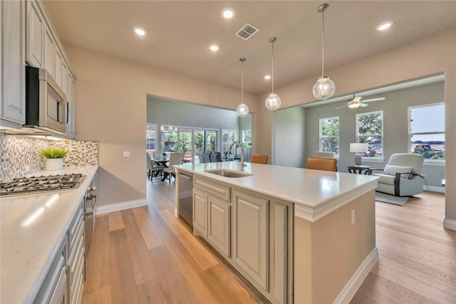 kitchen featuring stainless steel appliances, sink, light wood-type flooring, and a kitchen island with sink