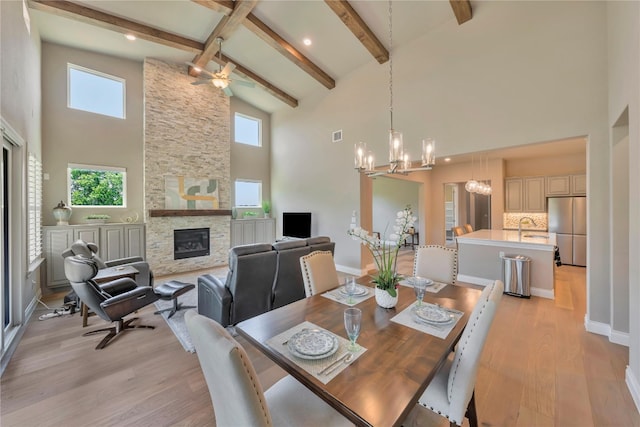 dining room with beam ceiling, high vaulted ceiling, a fireplace, and light wood-type flooring