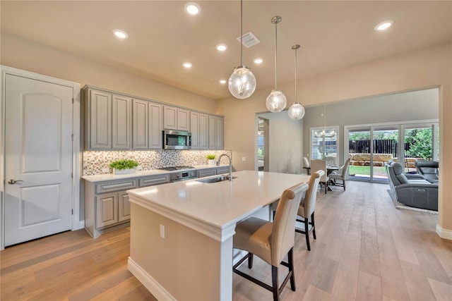 kitchen featuring hanging light fixtures, light wood-type flooring, an island with sink, sink, and tasteful backsplash