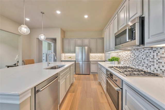 kitchen featuring light hardwood / wood-style flooring, backsplash, hanging light fixtures, appliances with stainless steel finishes, and sink