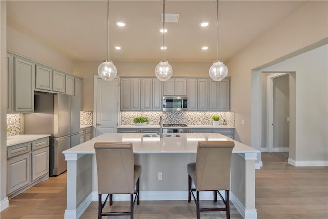 kitchen featuring stainless steel appliances, a center island with sink, light hardwood / wood-style flooring, and backsplash