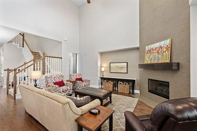 living room featuring a tiled fireplace, wood-type flooring, and a high ceiling