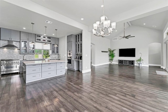 kitchen featuring wall chimney range hood, gray cabinetry, arched walkways, and appliances with stainless steel finishes