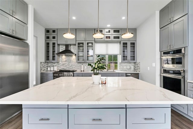 kitchen with wall chimney exhaust hood, a kitchen island, stainless steel appliances, and tasteful backsplash