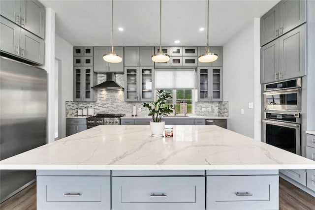 kitchen featuring tasteful backsplash, a center island, wall chimney range hood, appliances with stainless steel finishes, and gray cabinets