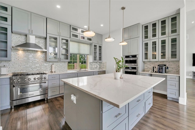 kitchen featuring a center island, wall chimney exhaust hood, light stone countertops, dark hardwood / wood-style flooring, and stainless steel appliances