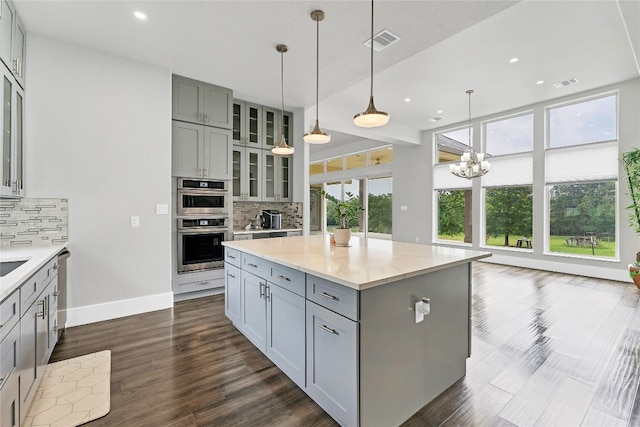 kitchen featuring gray cabinetry, decorative backsplash, a kitchen island, and decorative light fixtures