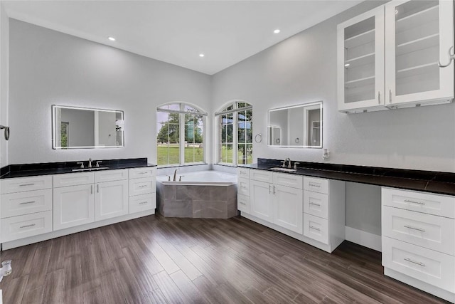 bathroom featuring two vanities, a bath, a sink, and wood finished floors