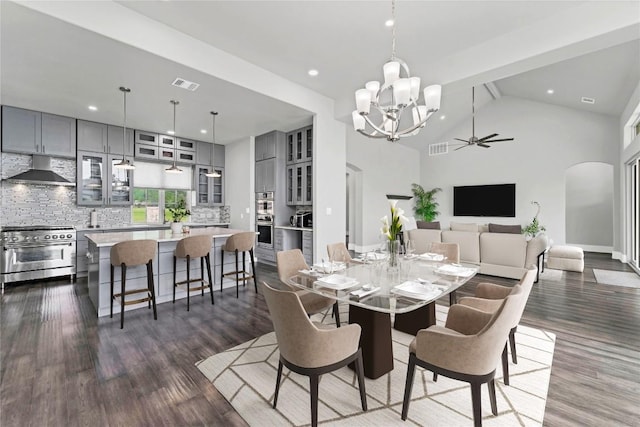 dining room with ceiling fan with notable chandelier, dark wood-type flooring, and high vaulted ceiling