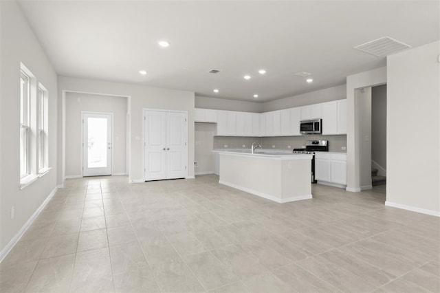 kitchen with a kitchen island with sink, white cabinets, sink, light tile patterned flooring, and stainless steel appliances