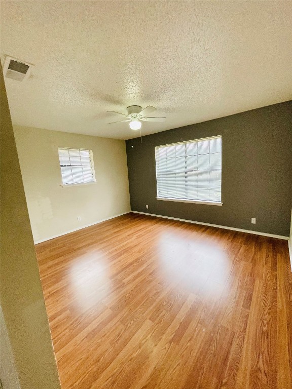 spare room with light wood-type flooring, a textured ceiling, a wealth of natural light, and ceiling fan