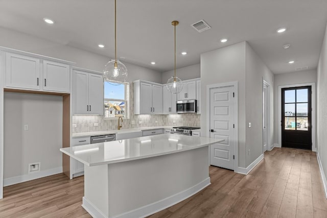 kitchen featuring white cabinets, appliances with stainless steel finishes, a kitchen island, and hanging light fixtures