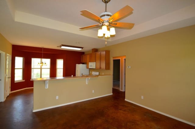 kitchen featuring white appliances, decorative light fixtures, ceiling fan with notable chandelier, a raised ceiling, and a kitchen bar