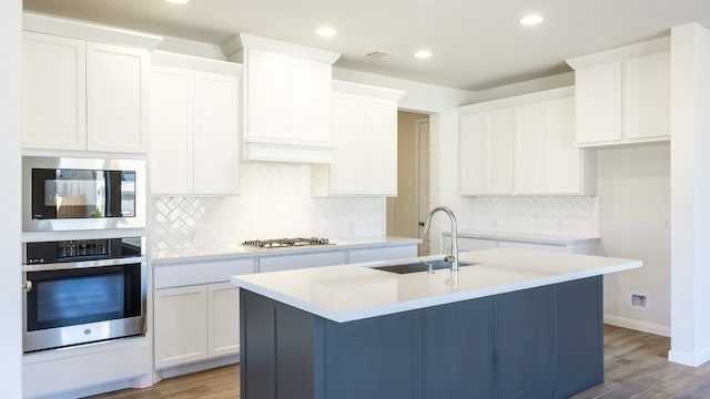 kitchen with appliances with stainless steel finishes, sink, white cabinetry, light hardwood / wood-style floors, and a center island with sink