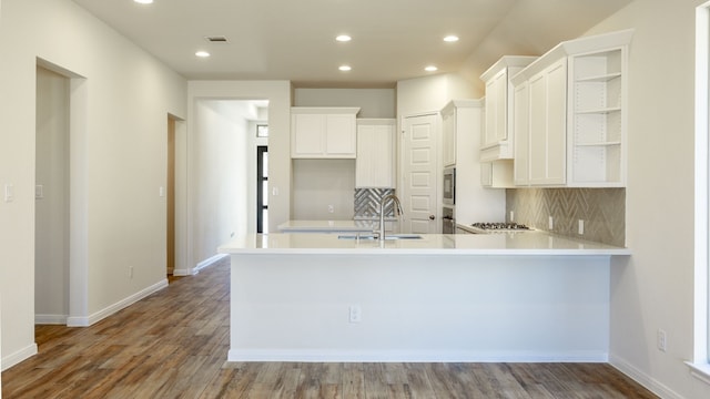 kitchen featuring hardwood / wood-style floors, white cabinets, sink, kitchen peninsula, and backsplash